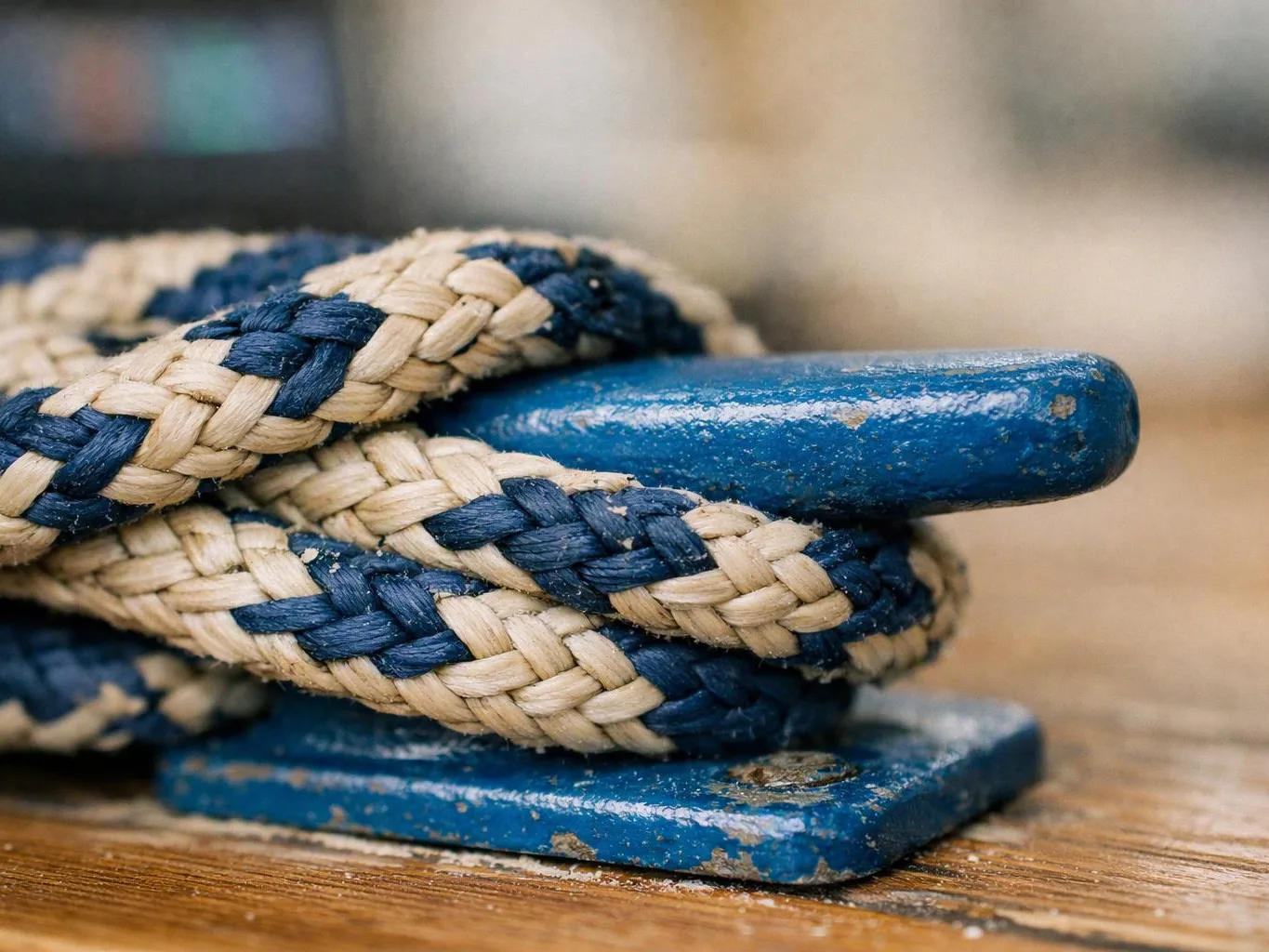 A blue and cream braided rope is wrapped around a weathered blue metal cleat on a wooden surface